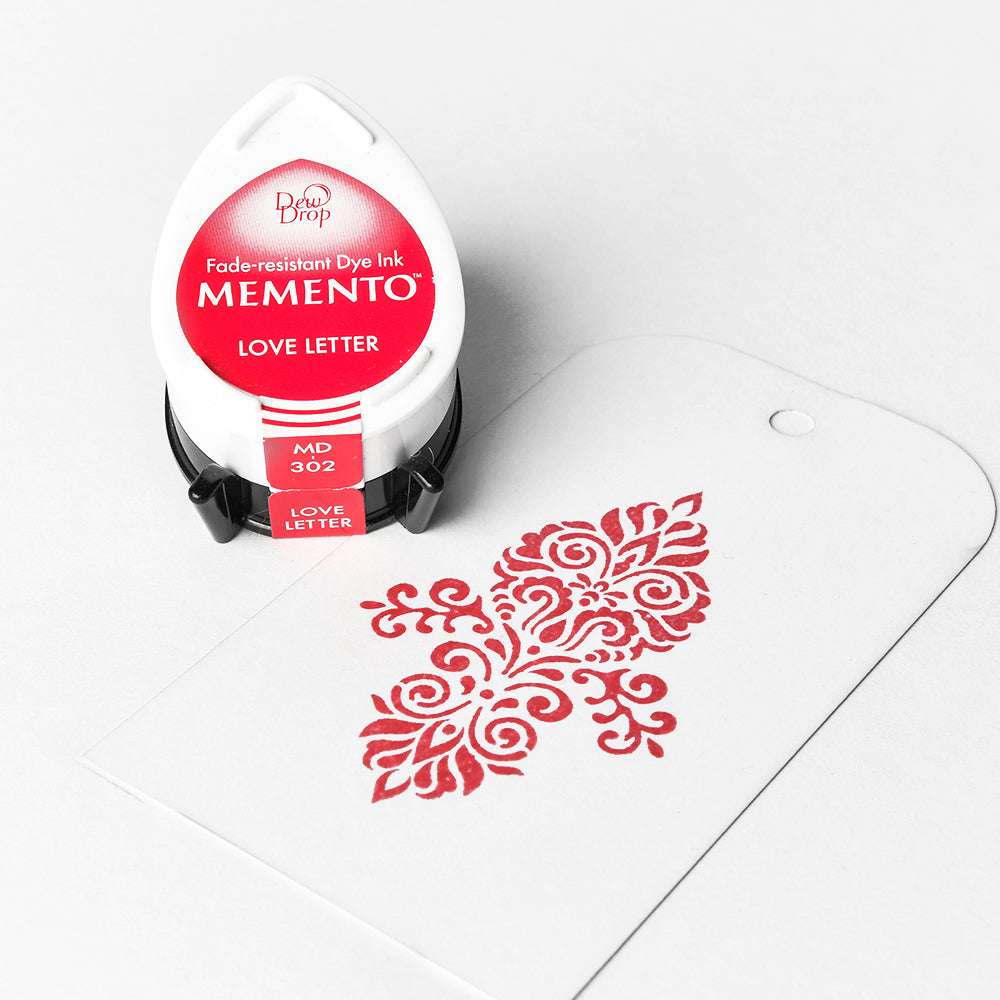 Tsukineko Memento Stempelkissen "Love Letter" neben einem weißen Anhänger mit roter Verzierung - ideal für gestochen scharfe Abdrücke und hochpigmentierte Farben.