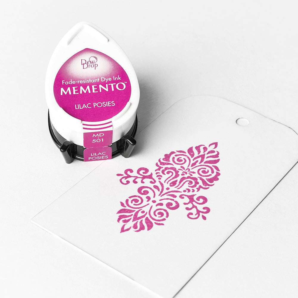 Ein rosafarbenes Memento Stempelkissen von Tsukineko und ein weißer Anhänger mit einem dekorativen rosafarbenen gestempelten Blumenmuster in hochpigmentierter Farbe.
