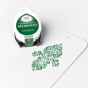 Ein Tsukineko Memento Cottage Ivy grünes Stempelkissen mit hochpigmentierter Farbe sitzt neben einem weißen Anhänger mit grünem Ziermuster.