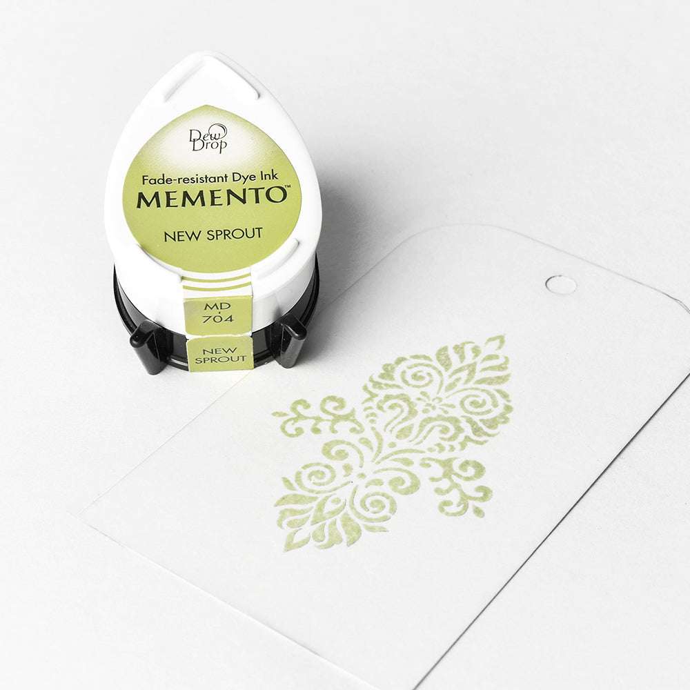 Ein Tsukineko Memento Stempelkissen "New Sprout" mit wasserbasierter Tinte liegt neben einem weißen Tag mit grünem Dekormuster.