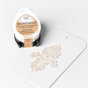 Tsukineko Memento Stempelkissen in Desert Sand neben einem weißen Tag mit dekorativem Muster - überzeugt mit hochpigmentierter, wasserbasierter Tinte.