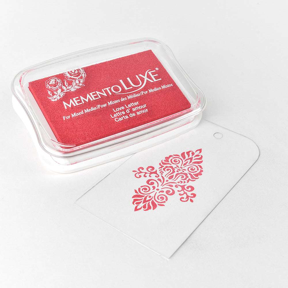 Tsukineko Memento Luxe Stempelkissen in Rot, gefüllt mit Pigment-Tinte, liegt neben einem weiß bestmpelten Anhänger-perfekt für Textilstempeln oder Papierbasteleien.