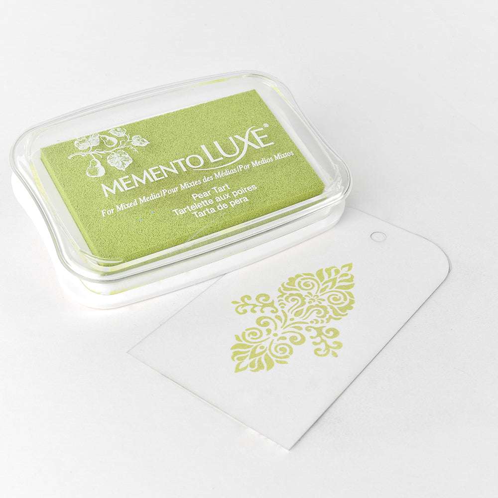 Das grüne Stempelkissen Tsukineko Memento Luxe Stempelkissen und der weiße Anhänger mit dem dekorativen grünen Stempelmotiv sind dank der satten Pigmenttinte des Kissens ideal für die Verwendung auf Stoffen.