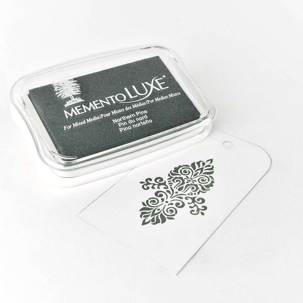 Das Tsukineko Memento LUXE Stempelkissen mit Pigment-Tinte liegt neben einem weißen Tag mit kunstvoll gestempeltem Kiefern-Muster - ideal zum Bestempeln von Stoff.