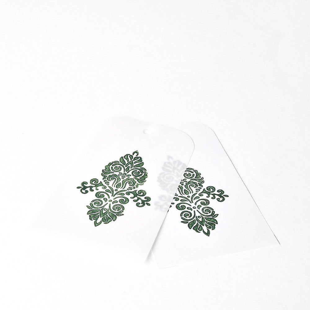 Zwei transparente Blätter mit verschlungenen grünen Blumenmustern, die sich auf weißem Hintergrund überlagern, unterstreichen die Eleganz der hochpigmentierten Tinte von Tsukineko und schaffen lebendige und bleibende Eindrücke.