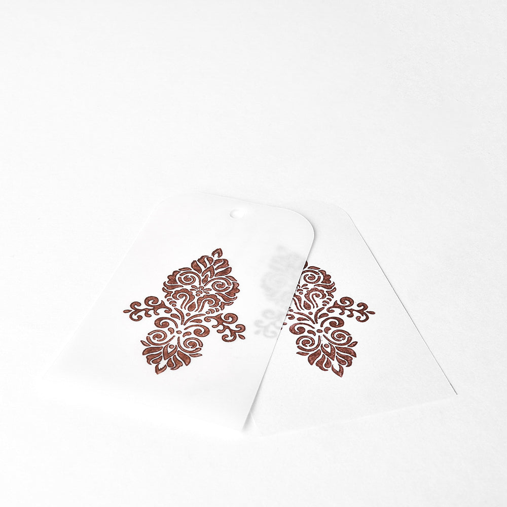 Zwei weiße Anhänger mit verschlungenen braunen Blumenmustern, hergestellt mit Tsukineko Brilliance Stempelkissen, überlappen sich auf weißem Hintergrund.