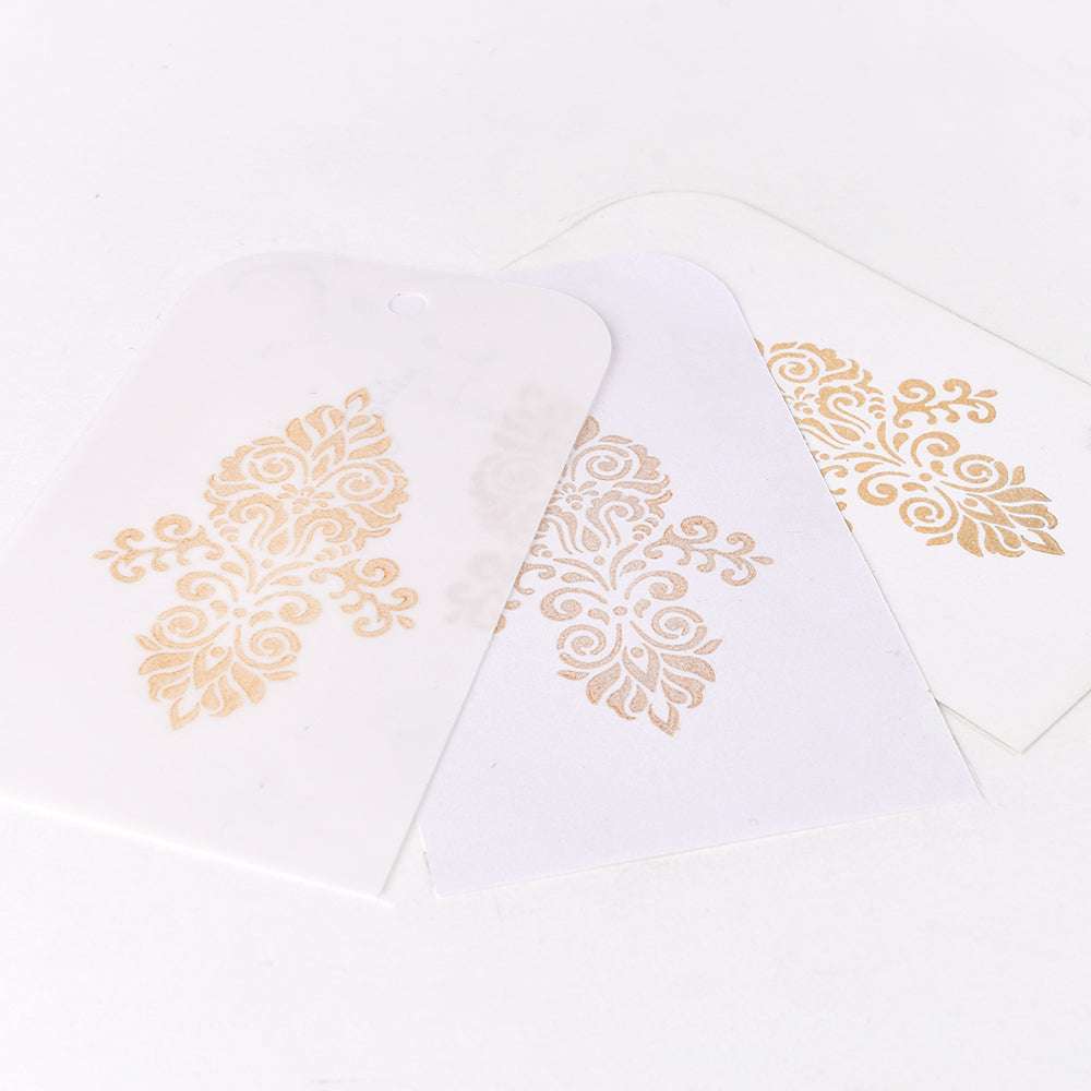 Drei weiße Karten mit goldenen Ornamenten, von denen eines durchscheinend ist und sich überlappt, zeigen metallische Effekte, die mit Tsukineko Delicata Mini Stempelkissen und wasserfester Tinte erzeugt wurden.