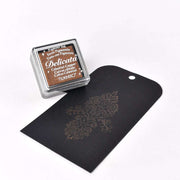 Ein Delicata Mini Stempelkissen in Kupfer von Tsukineko sorgt für metallische Effekte auf schwarzem Papier, das mit wasserfester Tinte und glänzendem Blumendesign gestaltet ist.