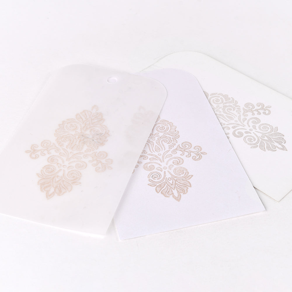 Drei weiße Karten mit verschnörkelten, goldfarbenen Blumenmustern überlappen sich auf weißem Hintergrund. Die Motive sind mit Tsukineko Delicata Mini Stempelkissen gestempelt, um einen exquisiten Metallic-Effekt zu erzielen.