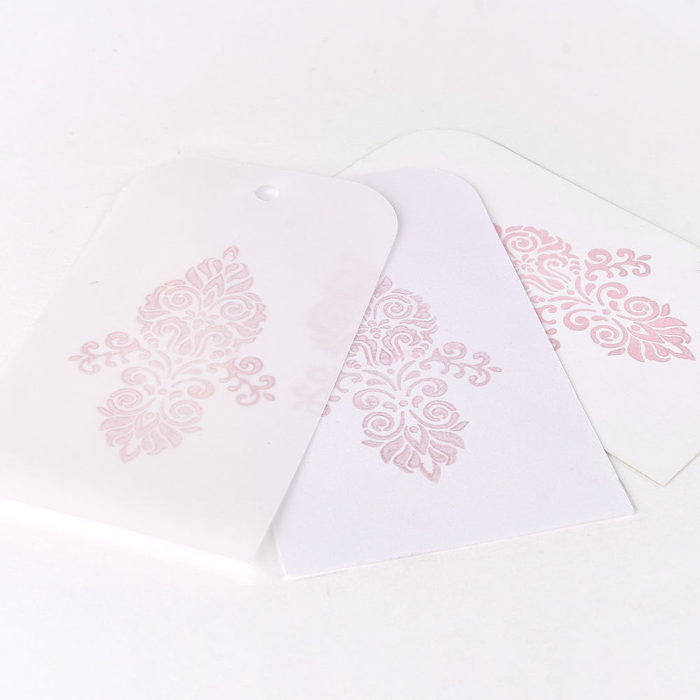 Drei weiße Anhänger mit hellrosa Ornamenten, hergestellt mit Tsukineko lichtechte Tinte für dauerhafte Schönheit, dargestellt auf weißem Hintergrund.