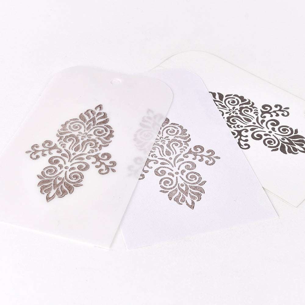 Eine dekorative Schablone erzeugt ein verziertes, symmetrisches Muster auf weißem Papier, das mit Tsukineko Delicata Mini Stempelkissen mit Metalleffekten veredelt wird.