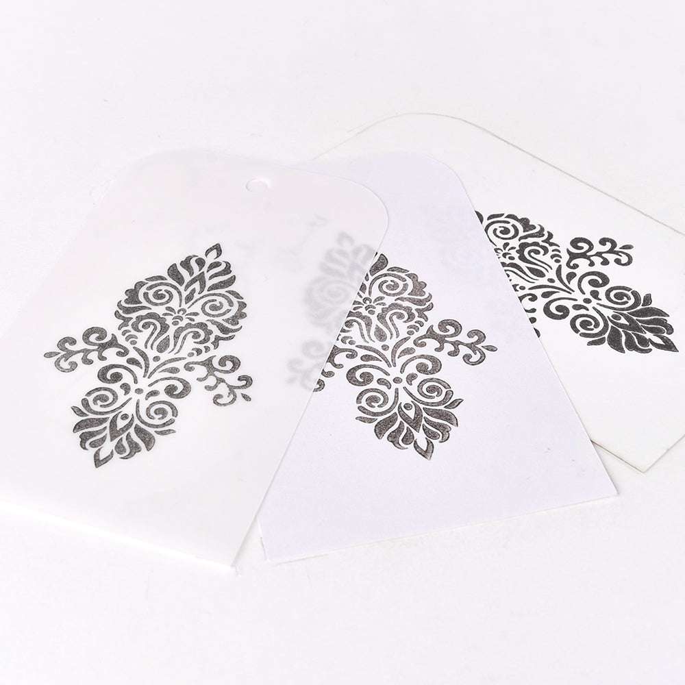 Drei transluzente Tsukineko-Schablonen mit verschnörkelten schwarzen Blumenmustern auf weißem Grund, leicht überlappend, mit lichtechten und wasserfesten Eigenschaften für dauerhafte Wirkung.