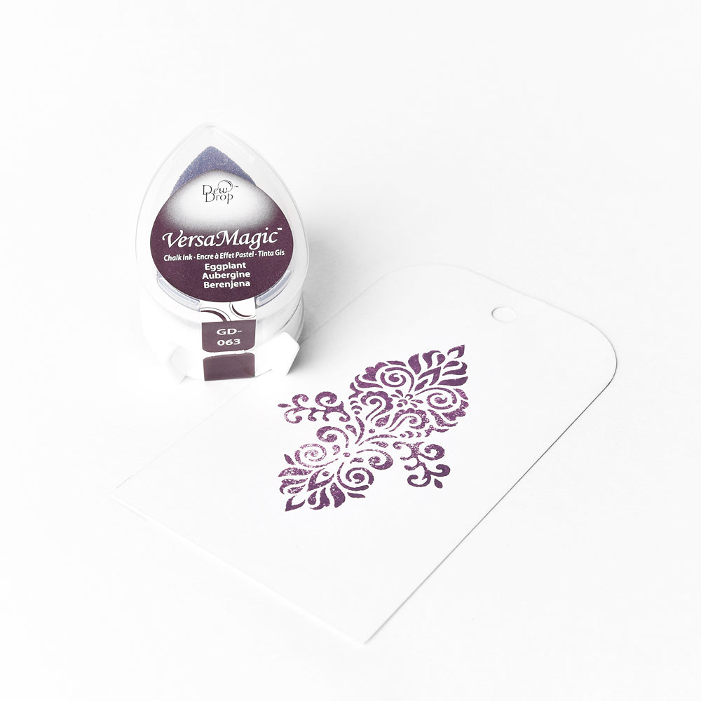 Ein Tsukineko VersaMagic Stempelkissen für glattes Papier und ein weißer Tag, bestmpelt mit wasserbasierter Pigment-Tinte in lila, ornamentalem Design auf weißem Hintergrund.