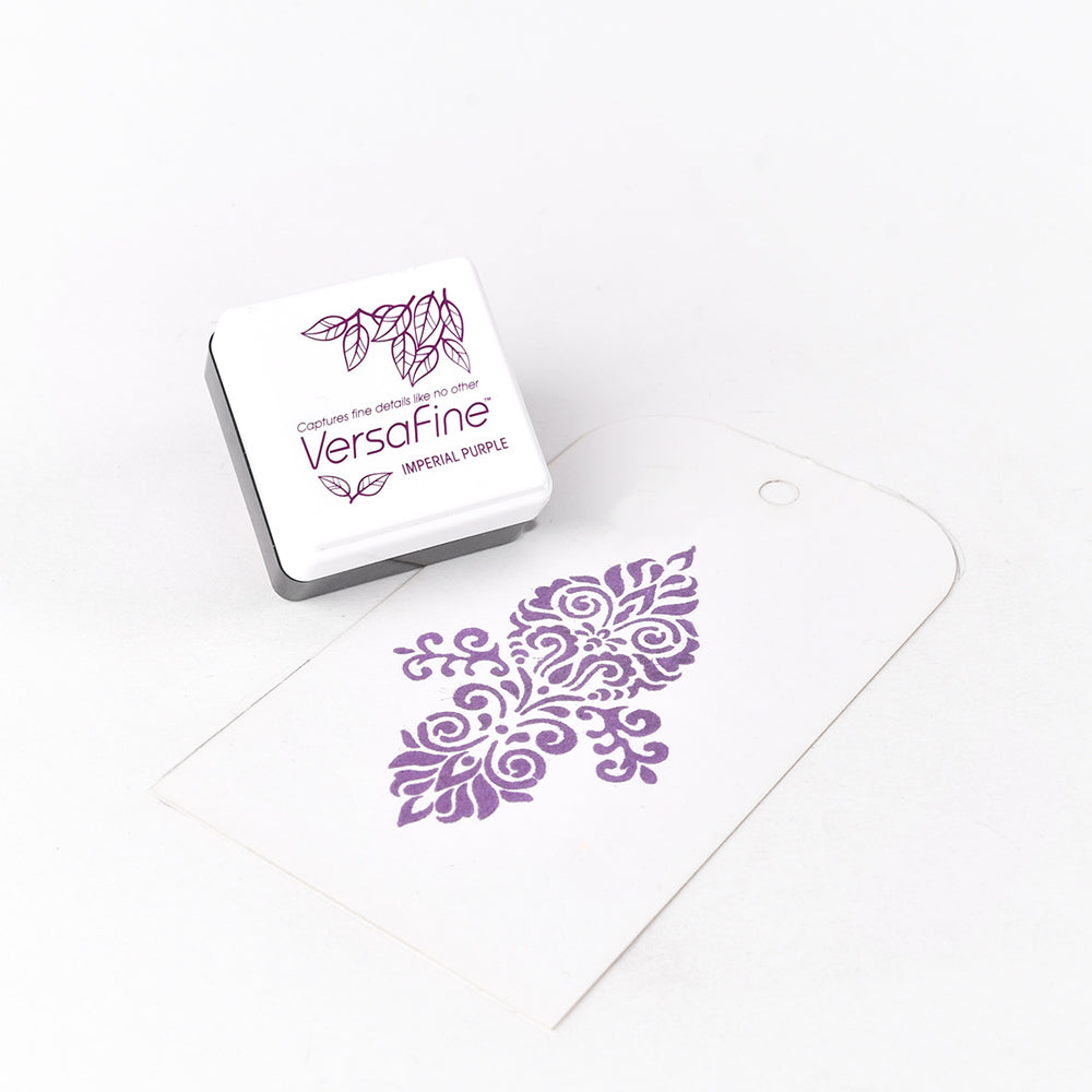 Die Tsukineko VersaFine Stempelkissen (klein) und ein weißer Anhänger, der mit einem lila Blumenmuster gestempelt ist, sind dank der satten Pigment-Tinte perfekt für feine Details.