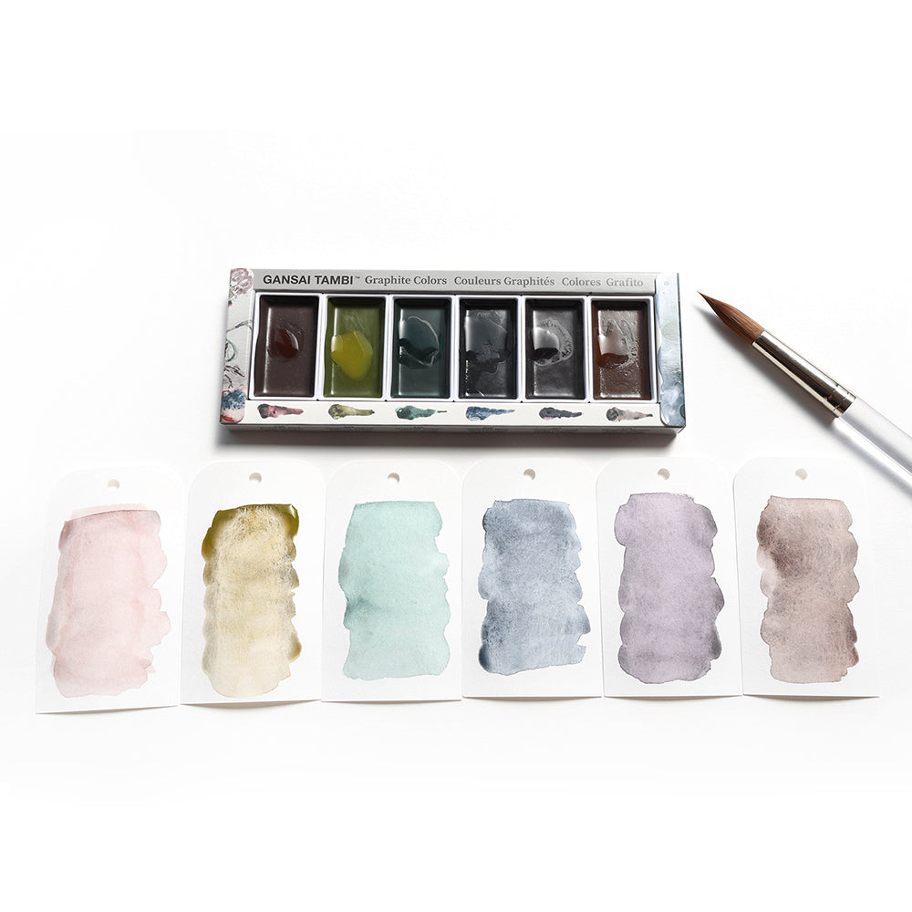 Sechs Kuretake Gansai Tambi Graphit-Aquarelltöpfe, ein Pinsel und fünf Farbfelder auf weißen Etiketten sind auf einem weißen Hintergrund angeordnet.