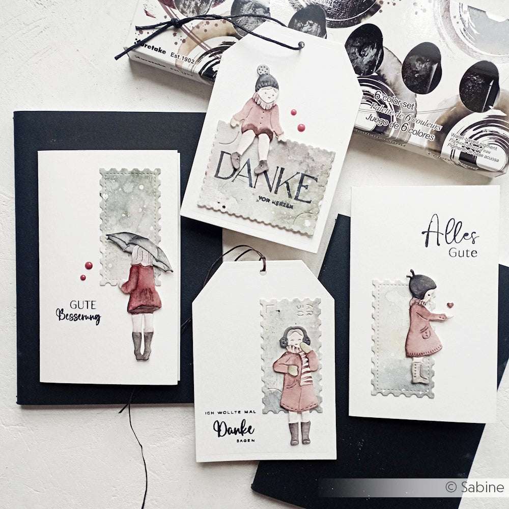 Vier handgefertigte Grußkarten mit Aquarell-Illustrationen von Mädchen und deutschen Botschaften, angeordnet auf einer weißen Oberfläche, mit zarten Details, gemalt mit Kuretake Aquarellfarben.