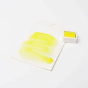 Ein Stück gelbe Aquarellfarbe von Rico Design Künstler Aquarellfarben auf Papier liegt neben einem passenden Gefäß und zeigt die leuchtenden Pigmente.