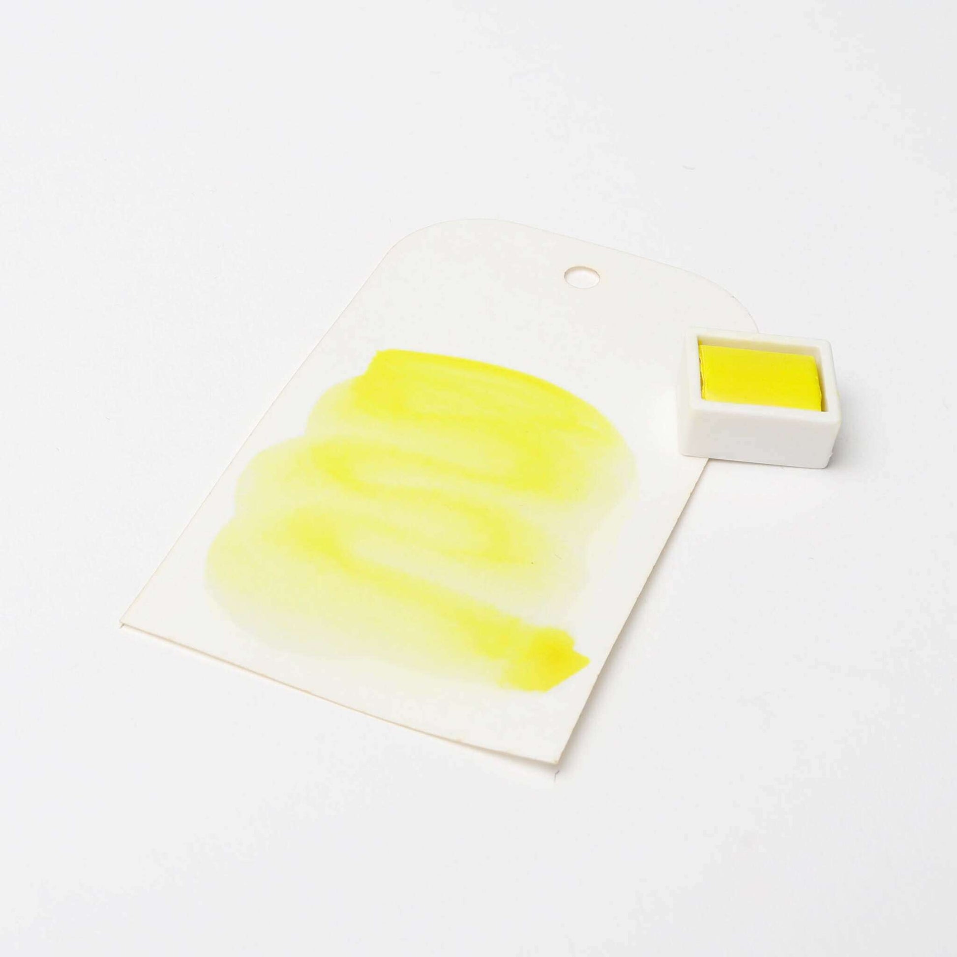 Ein Stück gelbe Aquarellfarbe von Rico Design Künstler Aquarellfarben auf Papier liegt neben einem passenden Gefäß und zeigt die leuchtenden Pigmente.