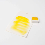 Ein weißes Schild mit gelben Aquarellfarben, auf dem Rico Design Künstler Aquarellfarben anpreist, steht neben einem kleinen quadratischen Topf mit gelber Aquarellfarbe.