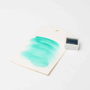 Ein Rico Design-Anhänger zeigt ein aquarellfarbenes Muster neben einem kleinen weißen Farbtopf, beide auf einem weißen Hintergrund.