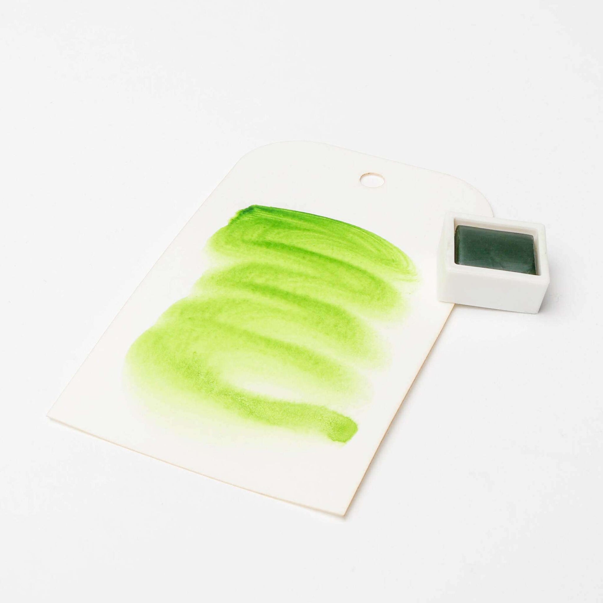 Ein grünes Aquarellmuster auf weißem Papier mit einem kleinen Schälchen Rico Design Künstler Aquarellfarben daneben, das die leuchtenden Pigmente und den gleichmäßigen Auftrag der Aquarellfarbe hervorhebt.