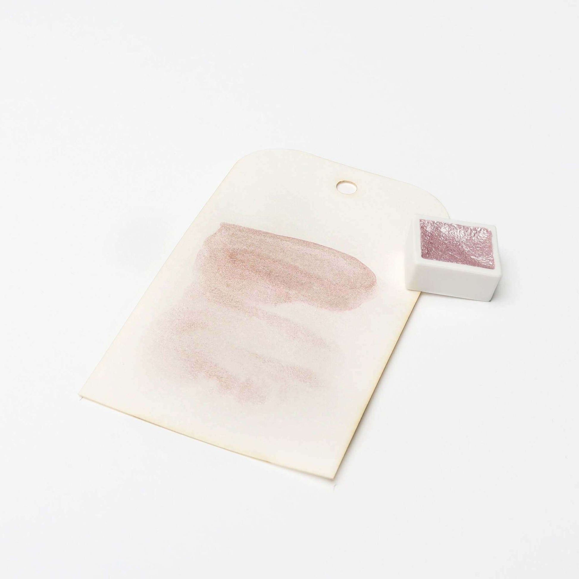 Ein kleiner rosa Aquarelltopf von Rico Design mit hochkonzentrierten Pigmenten ist neben einem Farbmuster auf einem weißen Anhänger mit Loch abgebildet.