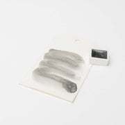 Ein schwarzer Aquarelltopf von Rico Design steht auf einem weißen Hintergrund neben einem Farbmuster mit schwarzen Pinselstrichen aus hoch konzentrierten Farbpigmenten.