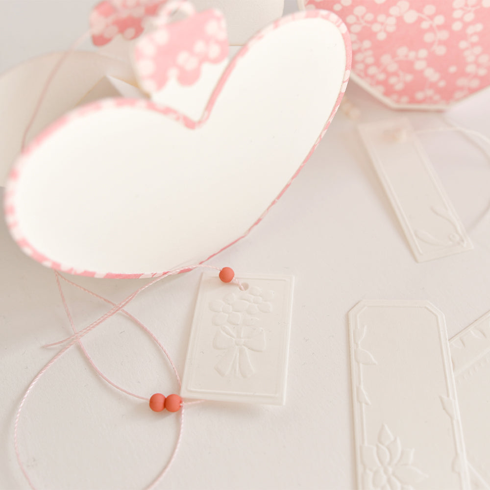 Geschenkanhänger aus Papier in Herzform mit Blumenprägung und rosa Schnur, hergestellt mit Stanz- und Prägevorlagen.