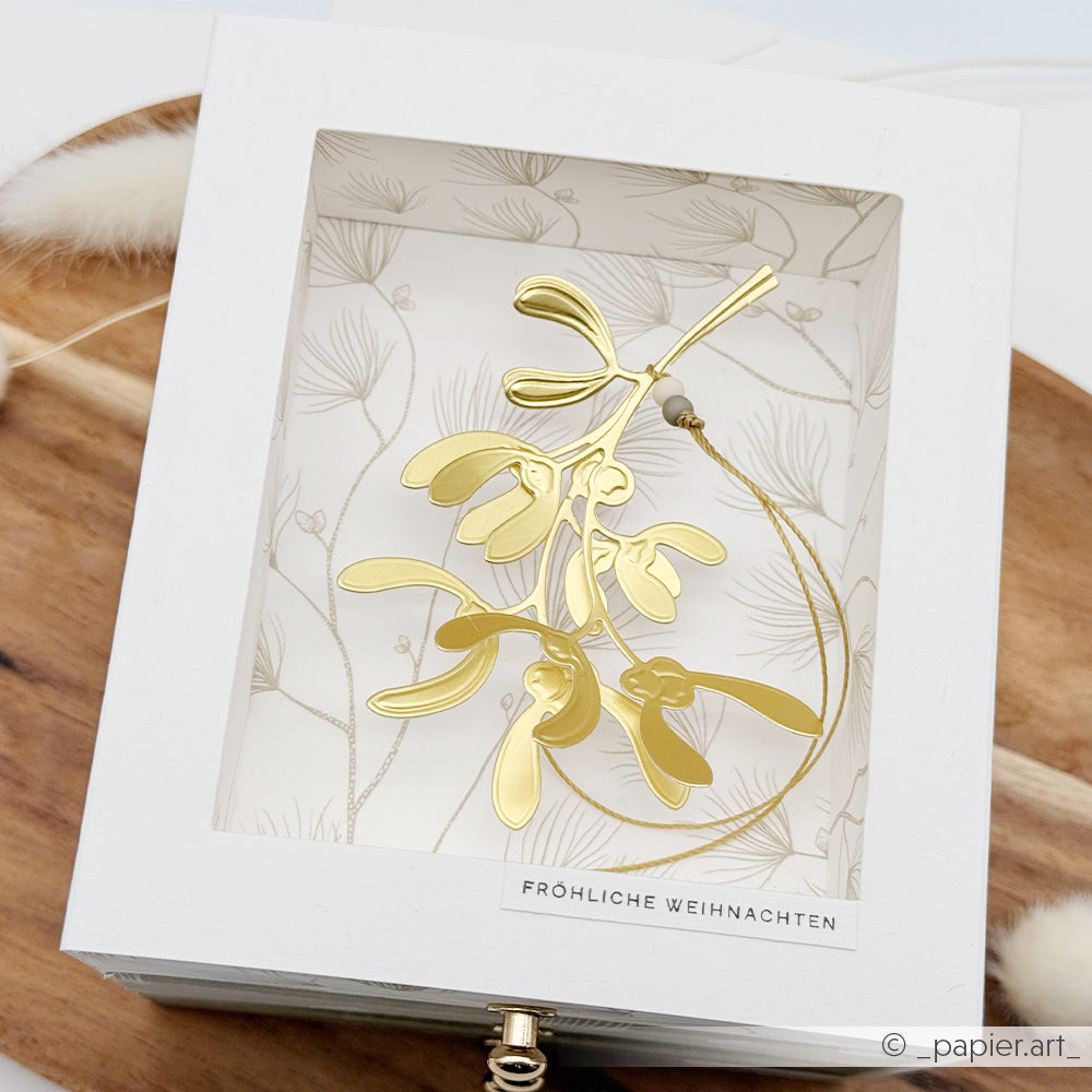 Goldfarbene Mistelzweig-Weihnachtskugel in einer Fröhliche Weihnachten-Schachtel, gestaltet mit den Stanzschablonen von Florale Etiketten.
