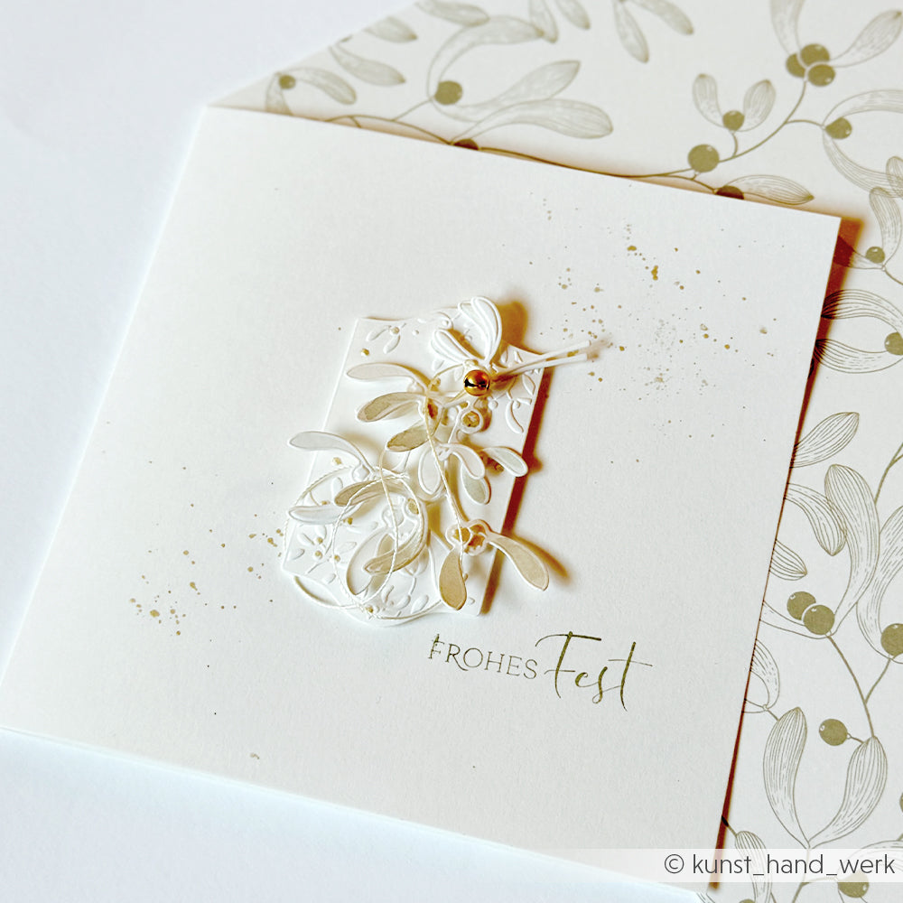 Eine quadratische Weihnachtskarte mit einem weißen Mistelzweig-Blumenetikett und dem Schriftzug FROHES Fest.