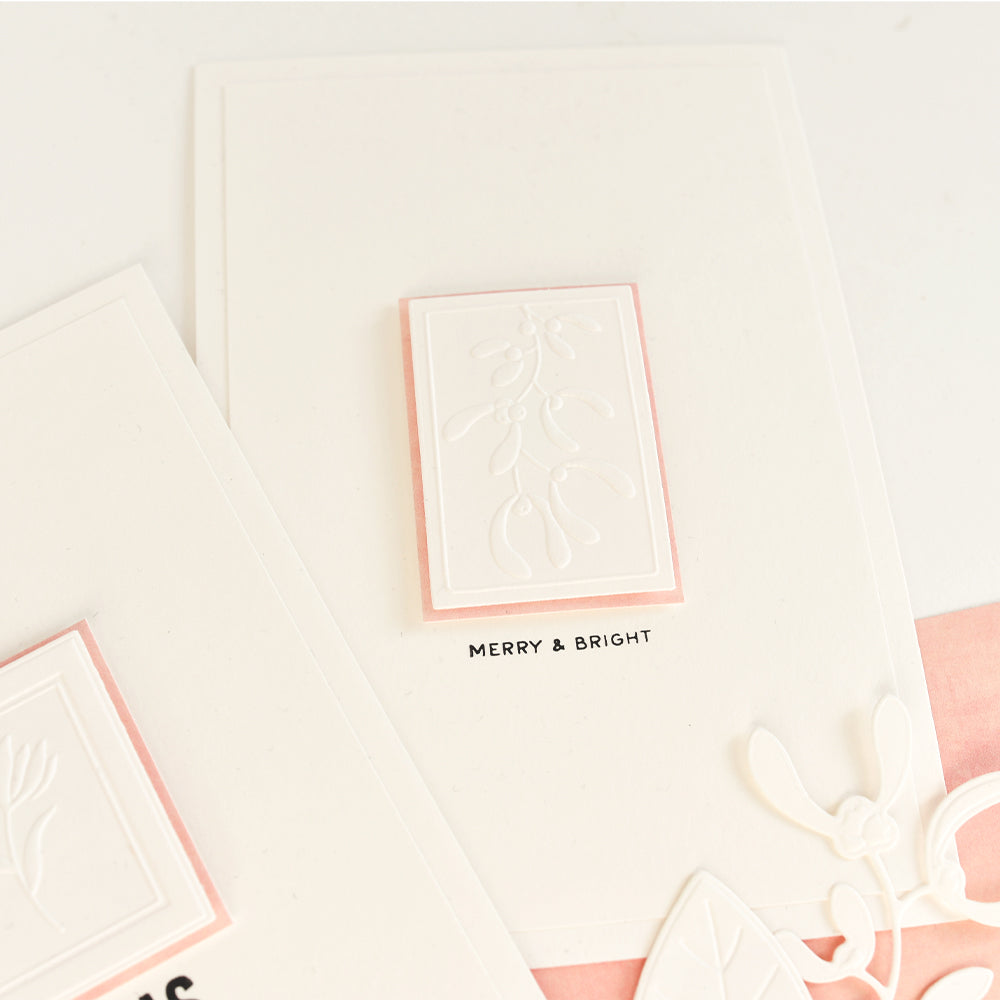 Handgefertigte Grußkarten mit Blumenetiketten mit Mistelzweigen und dem geprägten Schriftzug „MERRY & BRIGHT“.