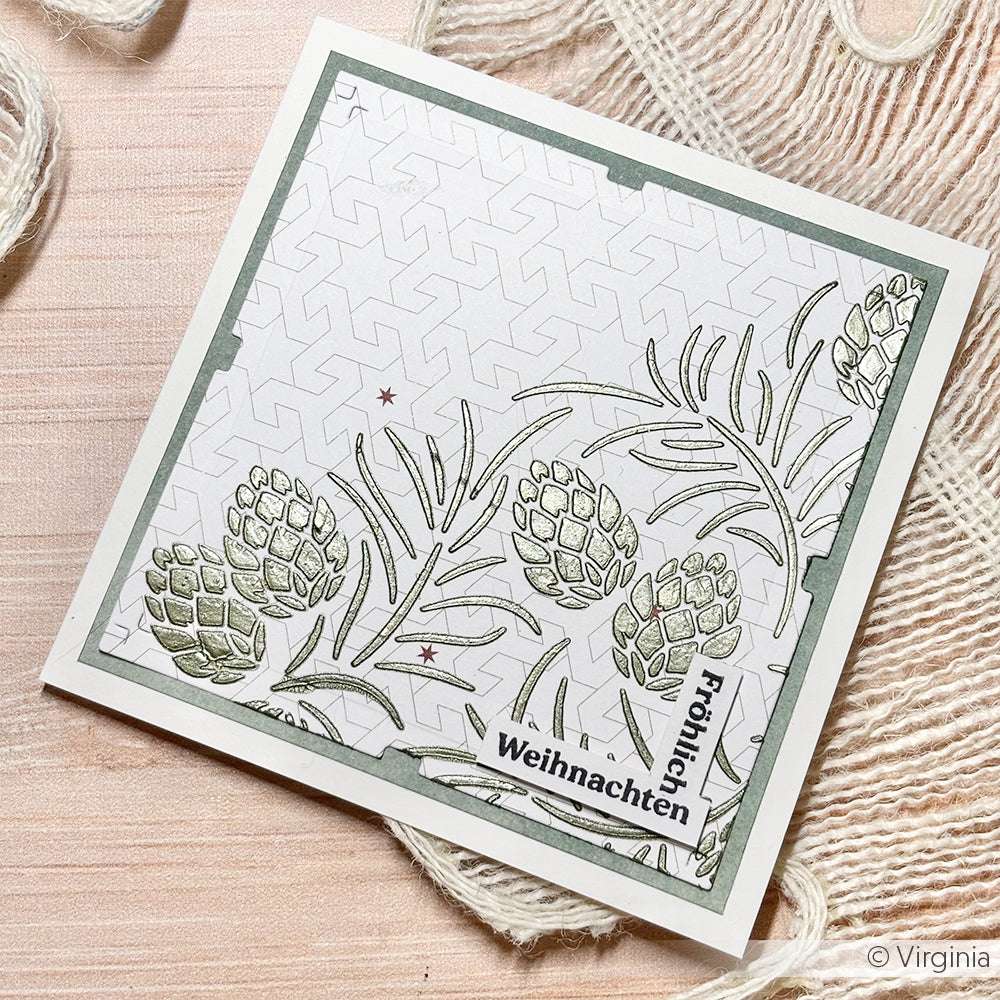 Quadratische Weihnachtskarte von Alexandra Renke mit Tannenzapfen, Tannennadeln und "Fröhliche Weihnachten" auf einem strukturierten Hintergrund - ideal für Papierprojekte oder als Inspiration für Schablonen-Designs.