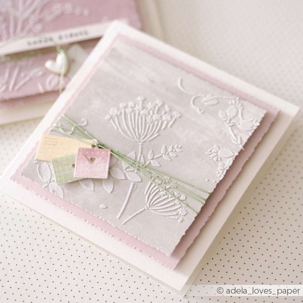 Handgefertigte Grußkarte mit geprägtem Blumenmuster, pastellfarbenen Anhängern und grüner Rankenschleife auf rosa und weißen Lagen - hergestellt mit Alexandra Renke Schablonen Papierprojekten für eine zarte Note.