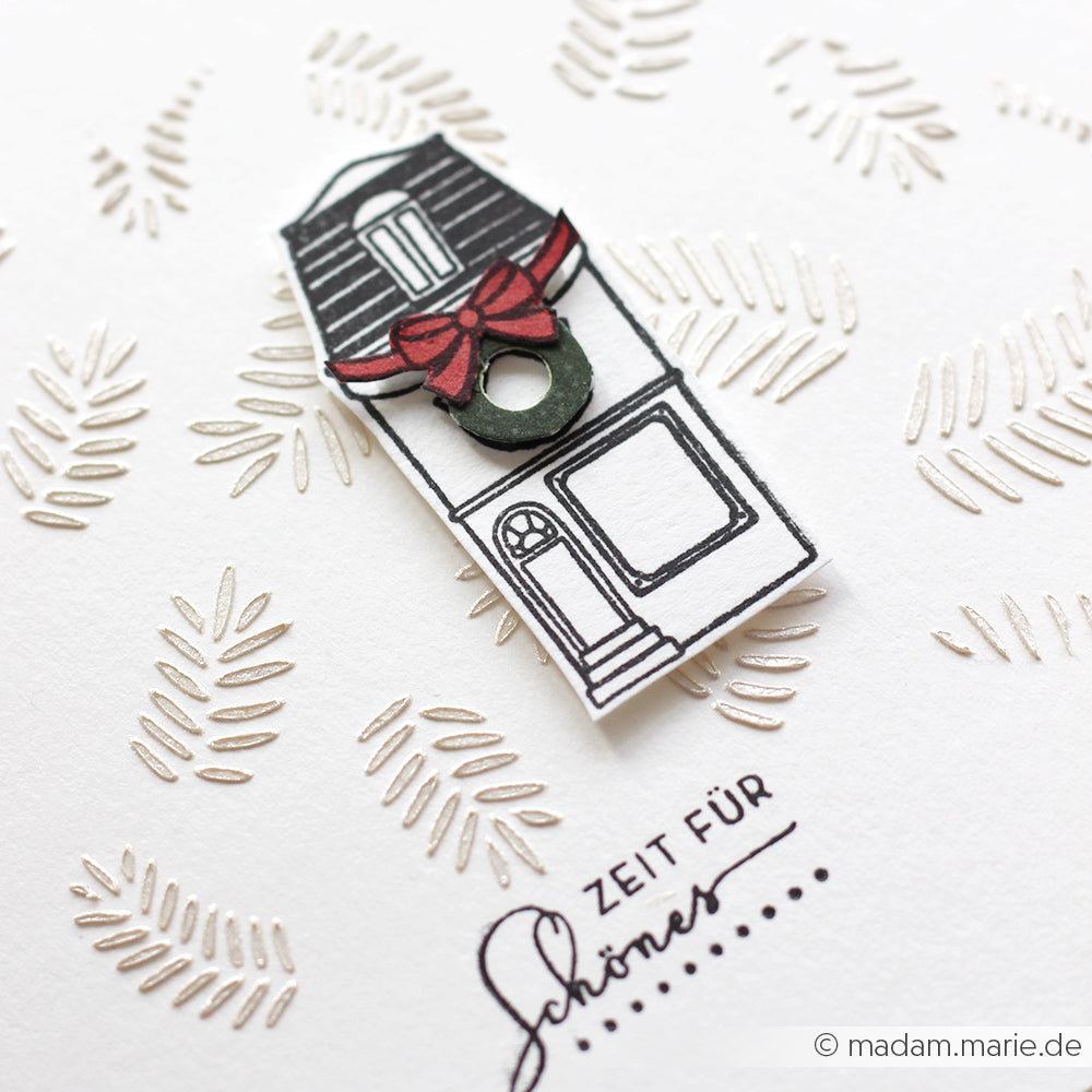 Handgefertigte Karte von Alexandra Renke mit schwarz-weißem Haus, roter Schleife, Text "Zeit für Schönes" und gemustertem Hintergrund mit Schablonendetails und Stencil Tannenzweige-Muster für eine charmante Note.