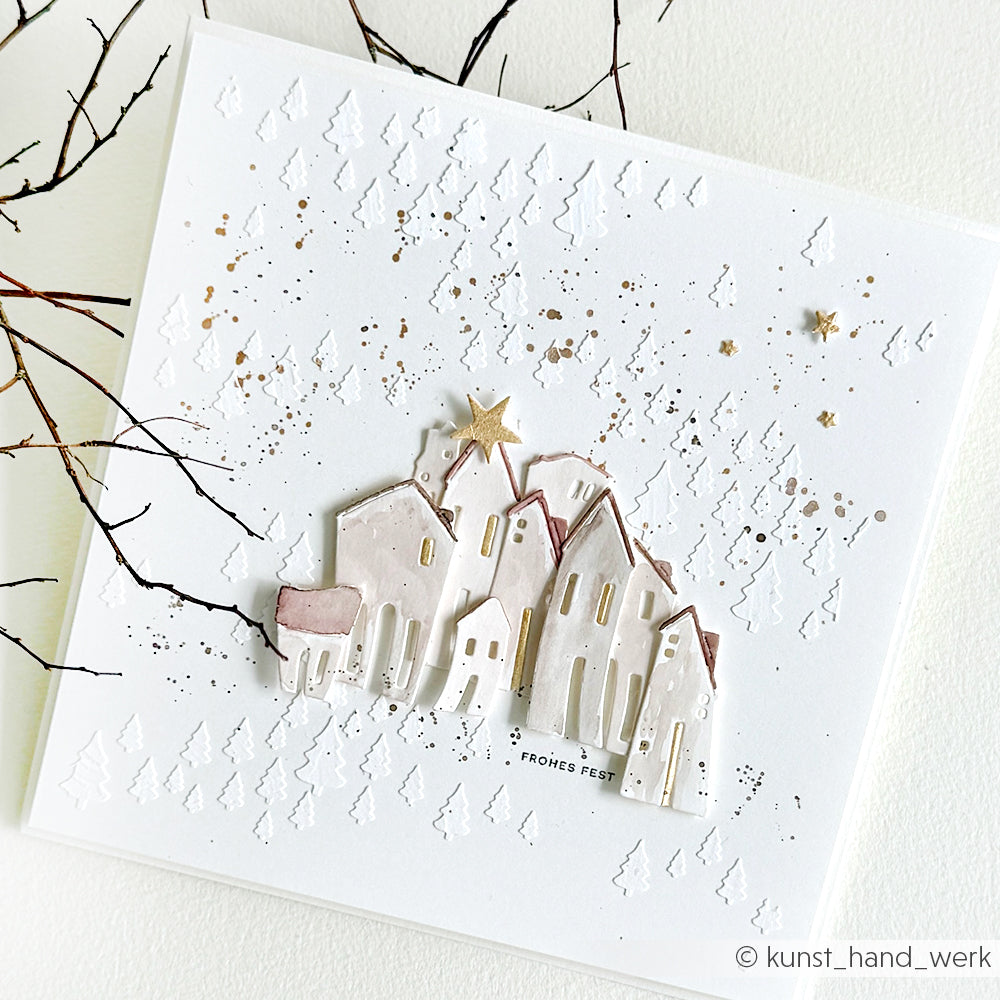Handgefertigte Weihnachtskarte mit pastellfarbenen Häusern, einem goldenen Stern und einer verschneiten Struktur - hergestellt mit den Schablonen von Alexandra Renke für Papierprojekte für einzigartige Details.