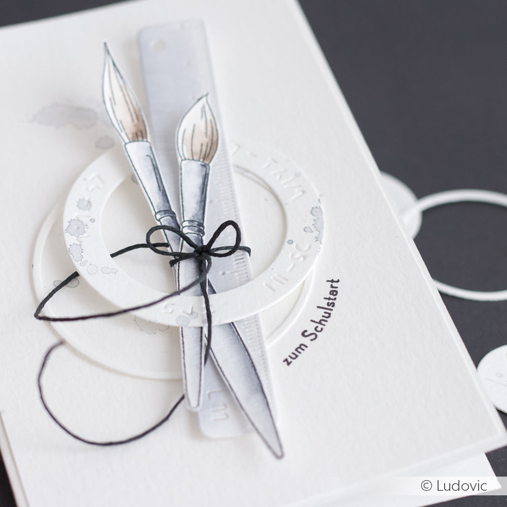 Handgefertigte Karte von Alexandra Renke mit illustrierten Pinseln, einem Lineal und einem Winkelmesser, die mit einem klaren Stempelset erstellt wurden, veredelt mit schwarzer Schnur auf weißem Hintergrund.