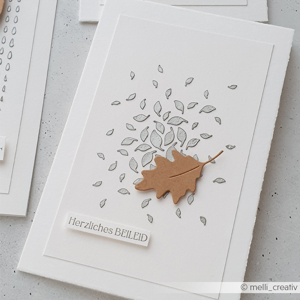 Weiße Beileidskarte mit verstreuten Blattmotiven und einem braunen Papierblatt, beschriftet mit „Herzliches BEILEID“ auf Deutsch. Diese liebevoll gestaltete Karte eignet sich ideal für Schablonen-Papierprojekte und besticht durch Motive, die mit wiederverwendbaren Schablonen gestaltet wurden – perfekt für alle, die Wert auf Details legen und Spaß am Schablonieren haben.