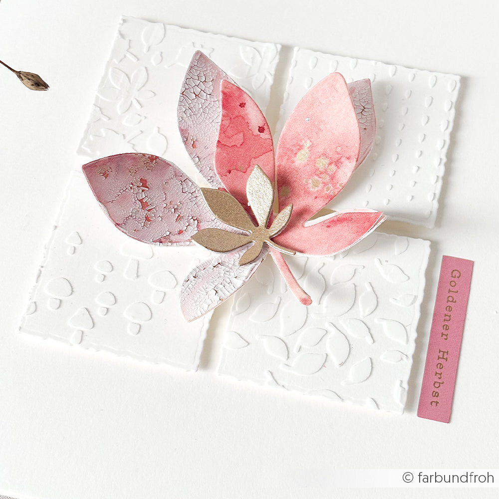 Ein rosa-goldenes Blatt in Aquarelloptik auf strukturiertem weißem Papier mit der Aufschrift „Goldener Herbst“ auf einem rosa Streifen, gestaltet mit der Schablone „Blätterspaß“ aus der Serie „Schablonen Papierprojekte“. Das Motiv verdeutlicht die zarte Wirkung wiederverwendbarer Schablonen und verleiht Ihren kreativen Projekten eine künstlerische Note.