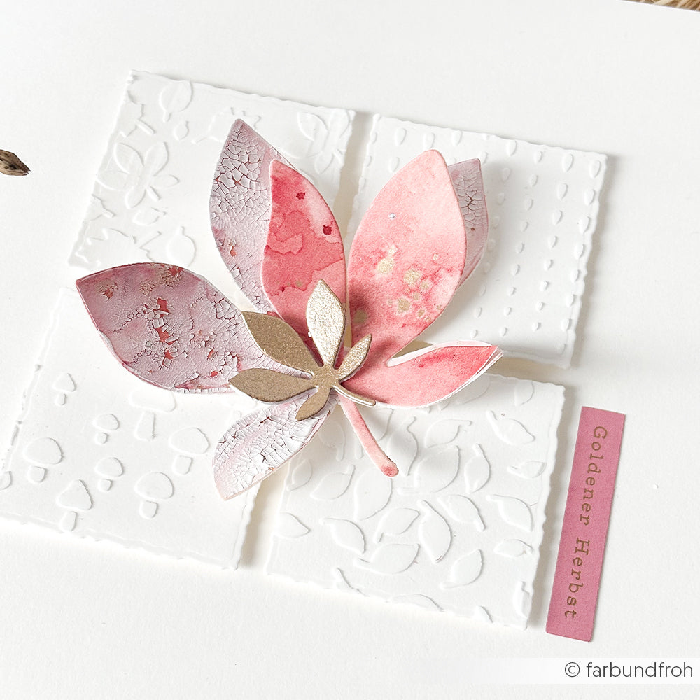 Papierkunstwerk mit einem rosa Blatt auf geprägten weißen Quadraten, rechts mit der Aufschrift „Goldener Herbst“ – perfekt ergänzt durch „wiederverwendbare Schablonen“, die zusätzliche kreative Möglichkeiten bieten.