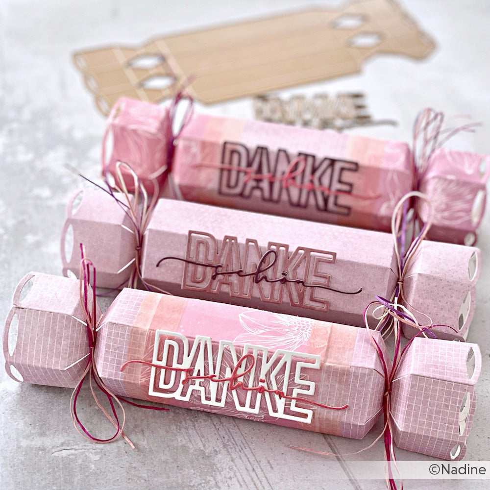 Drei rosafarbene Papiercracker, die mit Alexandra Renke Designpapieren hergestellt und mit der Motivstanze Knallbonbon verziert wurden, jeweils mit einer Schleife gebunden und auf einer hellen Fläche ausgestellt.