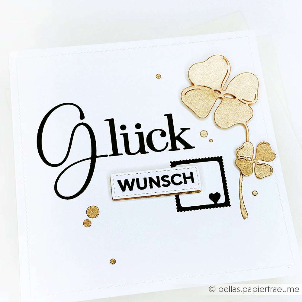 Weiße Karte von Alexandra Renke mit dem Schriftzug "Glückwunsch", elegant verziert mit goldenen Kleeblättern, die mit einer Kleeblattstanze detailgenau gefertigt wurden.