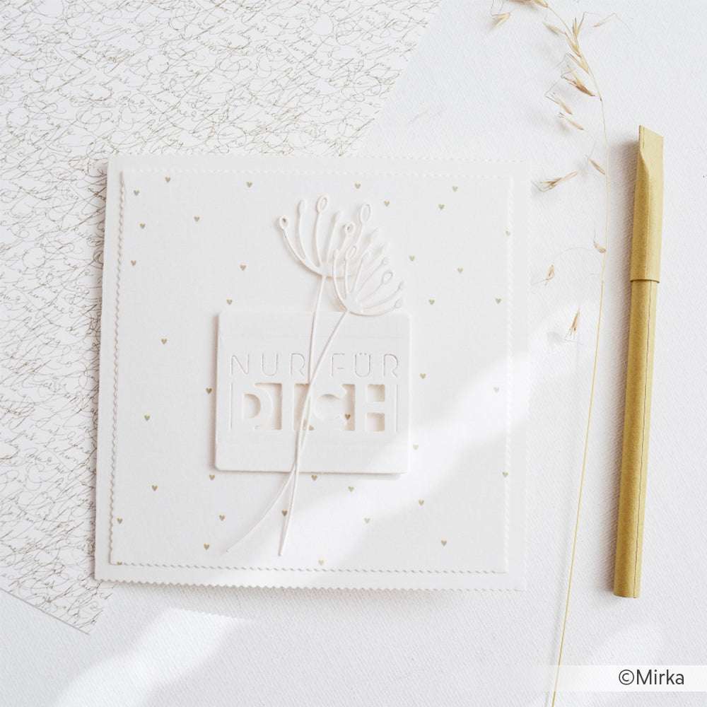 Quadratische weiße Karte mit dem Schriftzug "Nur für dich" und einem floralen Motiv, hergestellt mit feinen Stanzformen von Alexandra Renke, neben einem goldenen Stift und zartem getrocknetem Gras.