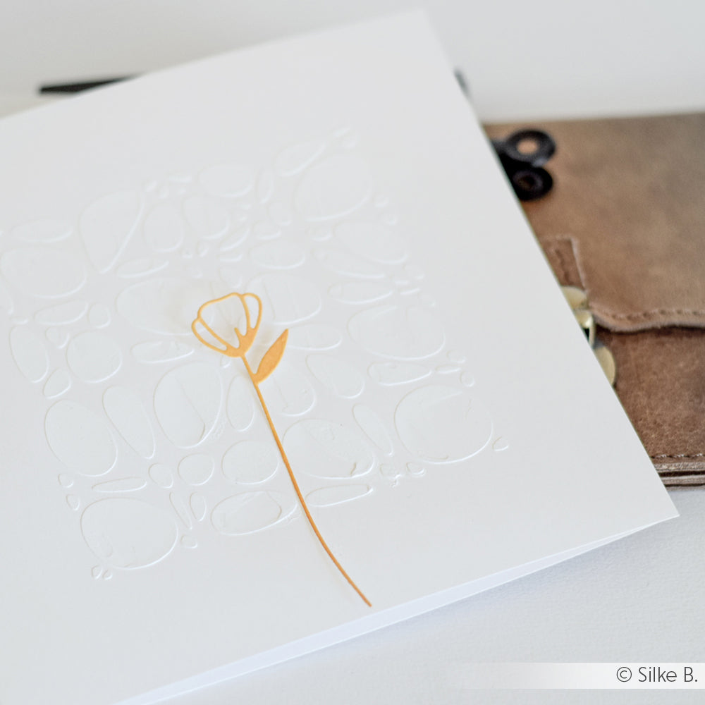 Minimalistische weiße Karte von Alexandra Renke aus Designpapier mit geprägten abstrakten Formen und einer einfachen gelben Blume, die mit der Artistblumen-Stanze hergestellt wurde, auf einer braunen Brieftasche.