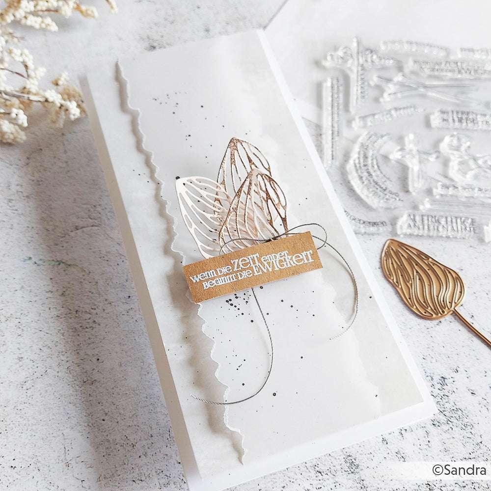 Handgemachte Karte von Alexandra Renke mit geschichtetem Papier, Metallic-Blättern, einem deutschen Zitat und schwarzen Spritzern auf Weiß - hergestellt mit detaillierten Stanzformen und Motivstanze für eine einzigartige künstlerische Note.