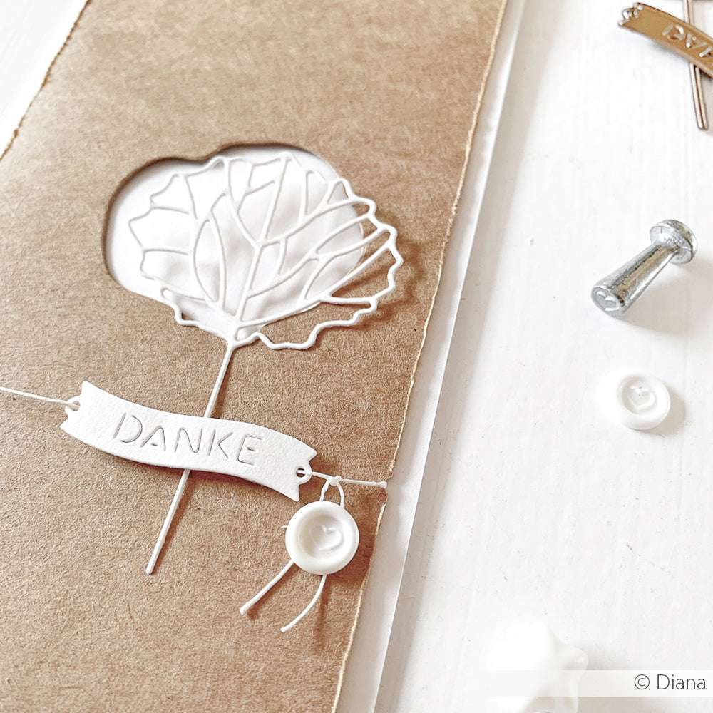 Handgemachte Karte mit einer zarten weißen Blume, die mit Alexandra Renke Motivstanze ausgeschnitten wurde, einem "Danke"-Banner auf braunem Papier und dekorativen Knöpfen daneben.