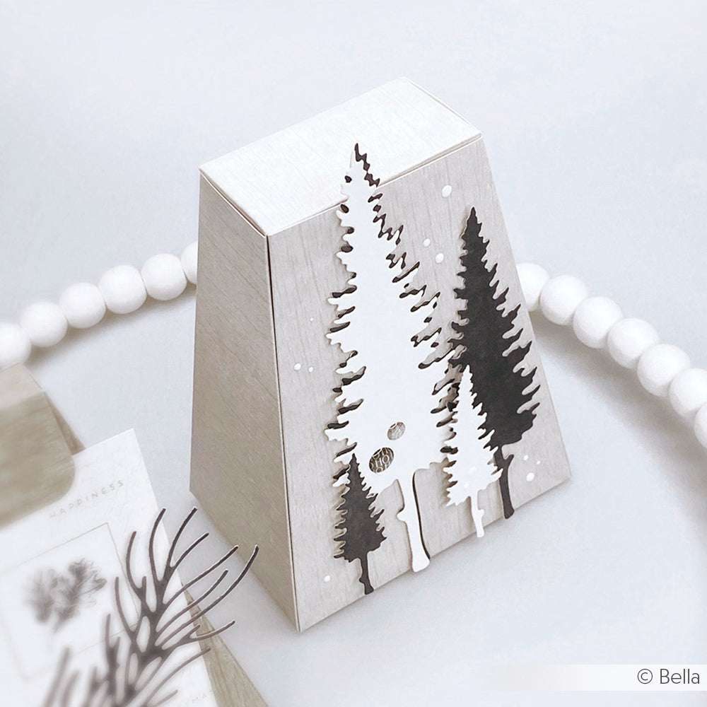 Eine silberne Schachtel mit Tannenbaumausschnitten, die mit den Motivstanze Fünf Tannen Set Dies von Alexandra Renke hergestellt wurde, steht auf einer weißen Fläche mit runden weißen Perlen im Hintergrund.