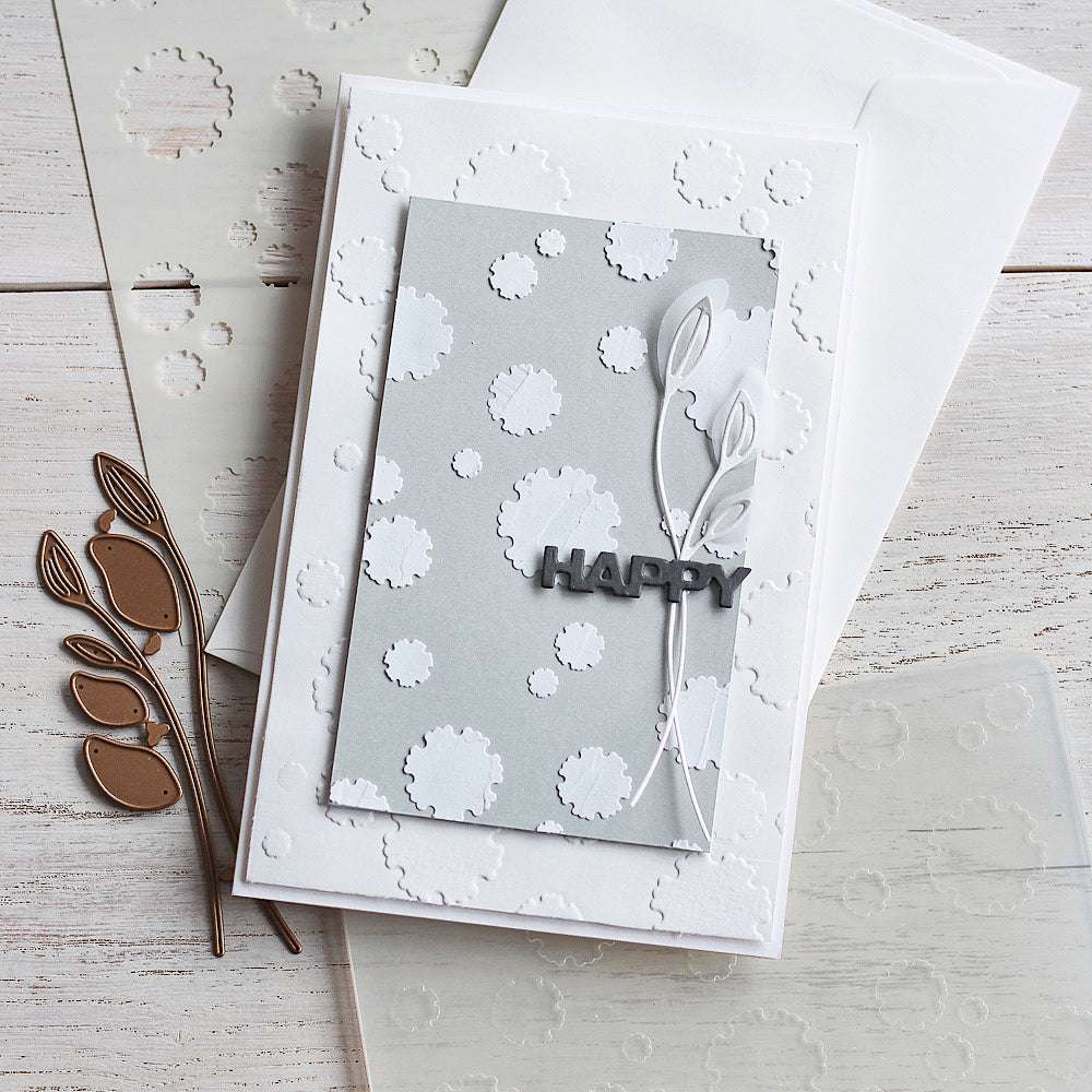 Eine handgefertigte Karte von Alexandra Renke mit dem Text HAPPY, weißen geprägten Punkten und zwei weißen Blattausschnitten auf einem grauen Paneel, hergestellt mit hochwertigem Designpapier und Motivstanze DieCut Systemen für ein elegantes Finish.