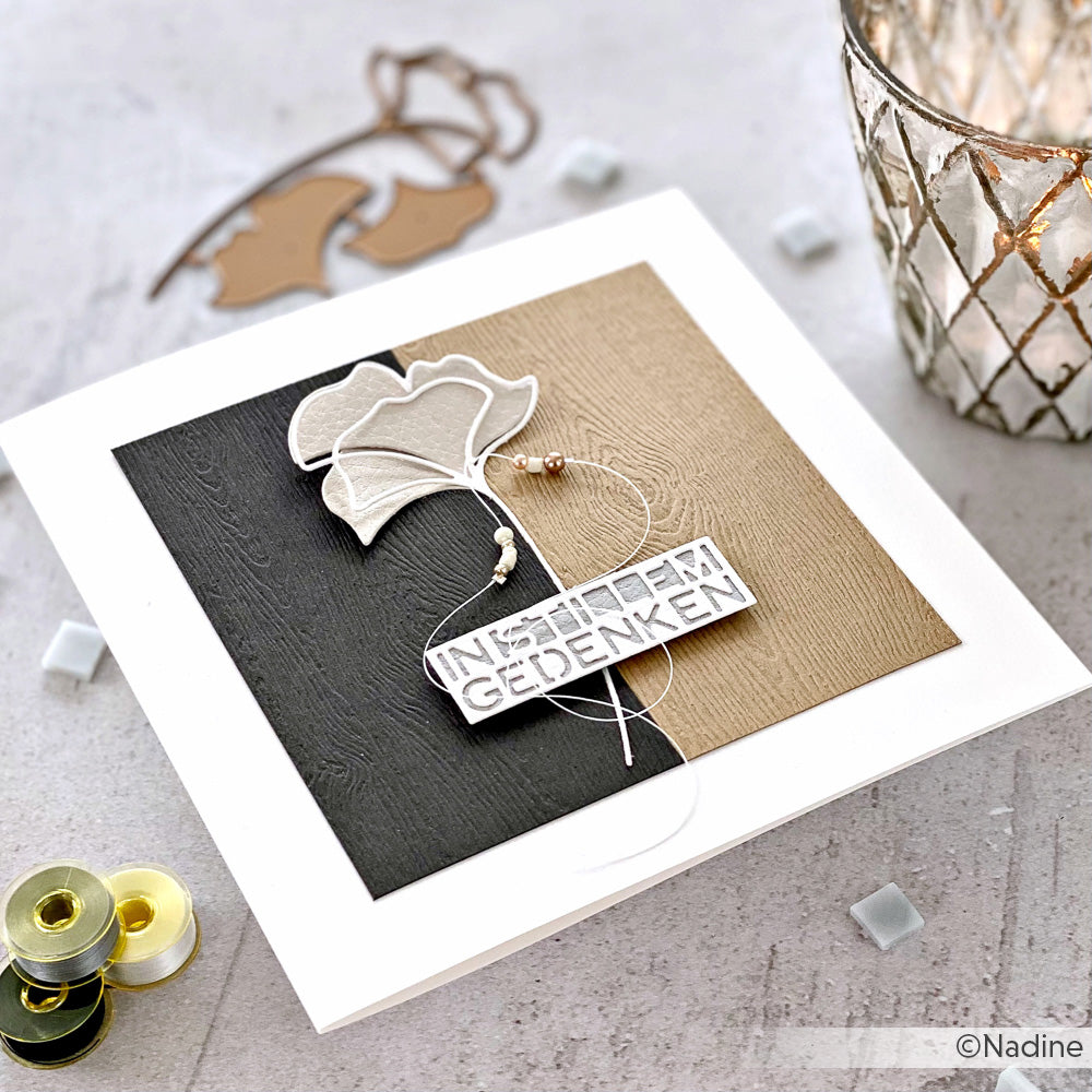 Quadratische Karte mit geschichteten Blumen, die mit den Stanzformen von Alexandra Renke hergestellt wurden, verziert mit Perlen, dem deutschen Text "In stillem Gedenken" und auf einem neutralen Hintergrund.