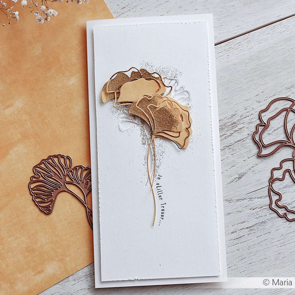 Handgefertigte Karte mit geschichteten goldenen Ginkgoblättern, die mit Alexandra Renke Stanzformen auf weißem Hintergrund hergestellt und auf einer hellen Holzoberfläche präsentiert wurden.