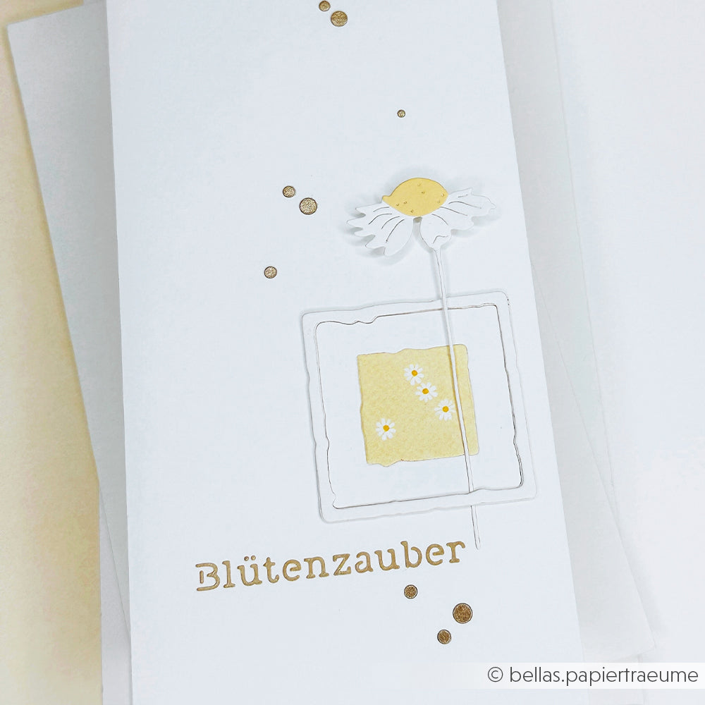 Weiße Karte mit goldenen Punkten, einer einfachen Blume, die mit der Alexandra Renke Motivstanze Margeriten-Paar gestanzt wurde, und Blütenzauber" in Gold am unteren Rand.